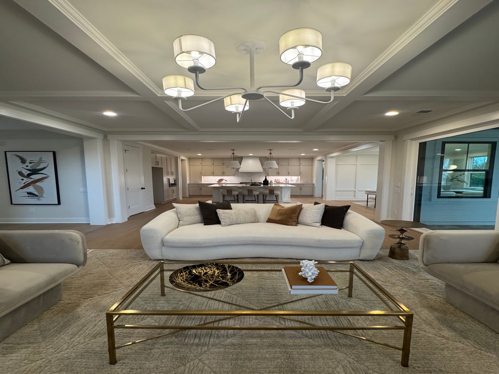 Open-concept living room with coffered ceiling, modern chandelier, and white curved sofa