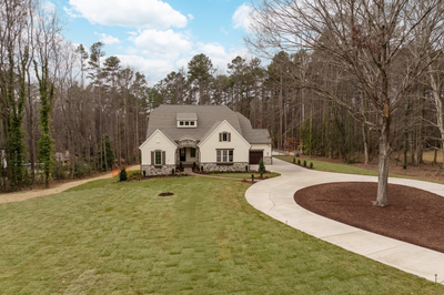 Single-story home with cream stucco exterior, stone accents, and curved driveway on wooded lot
