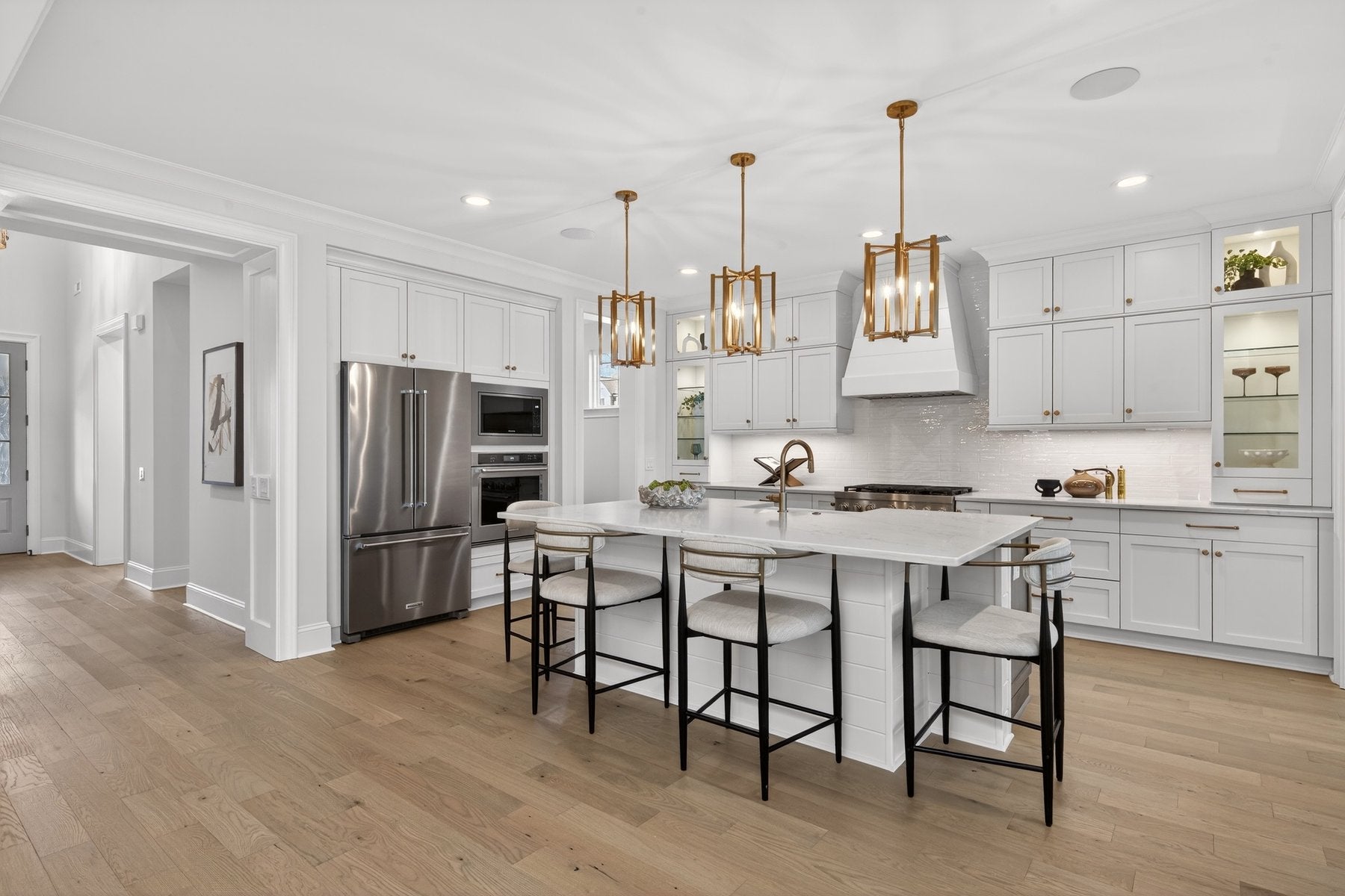 Modern white kitchen with large island, stainless appliances, and gold pendant lights