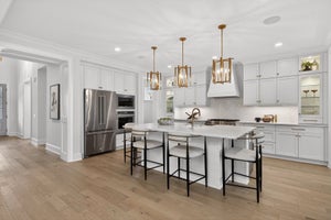 Modern white kitchen with large island, stainless appliances, and gold pendant lights
