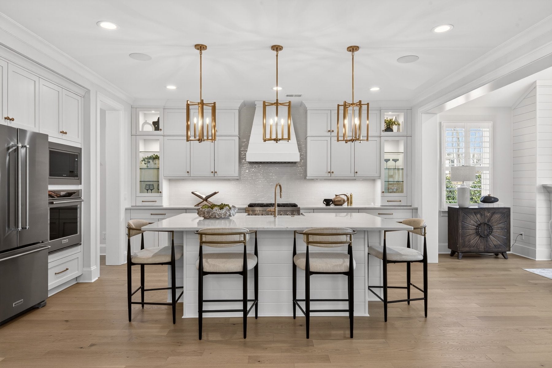 White kitchen with large island, gold pendant lights, and stainless steel appliances