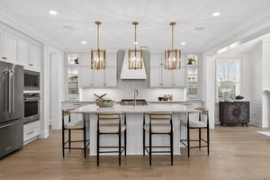 White kitchen with large island, gold pendant lights, and stainless steel appliances