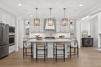 White kitchen with large island, gold pendant lights, and stainless steel appliances