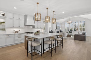 Open-concept kitchen and living room with white cabinets, island seating, and gold pendant lights