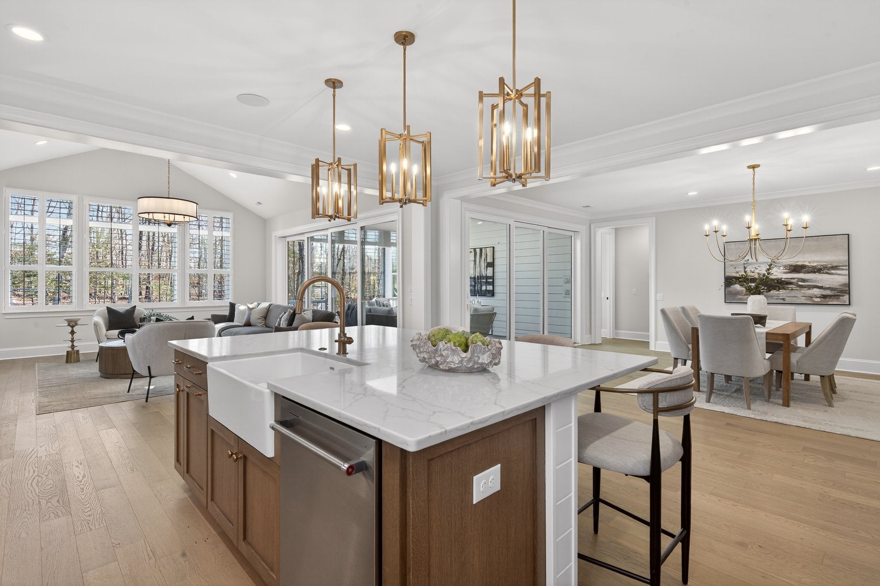 Open-concept kitchen with white island, gold pendant lights, and adjoining living and dining areas