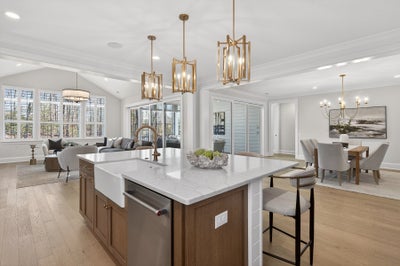Open-concept kitchen with white island, gold pendant lights, and adjoining living and dining areas