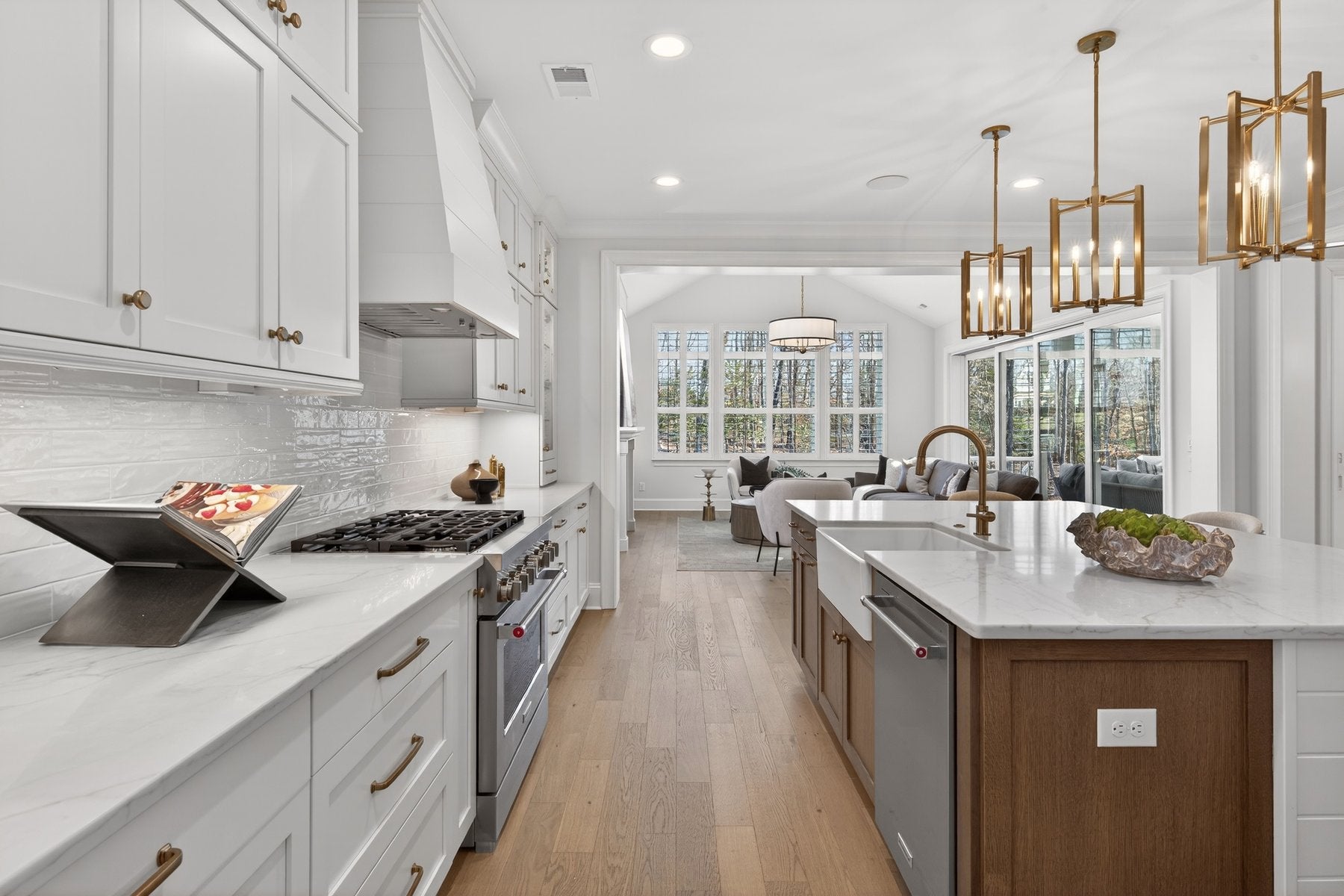 White kitchen with wood island, quartz countertops, gas range, and gold pendant lights overlooking living area