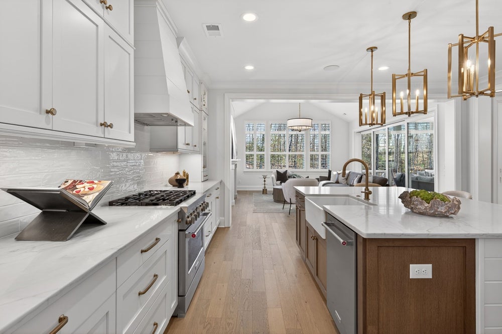 White kitchen with wood island, quartz countertops, gas range, and gold pendant lights overlooking living area