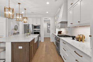 White kitchen with marble countertops, wood island, stainless appliances, and gold pendant lights