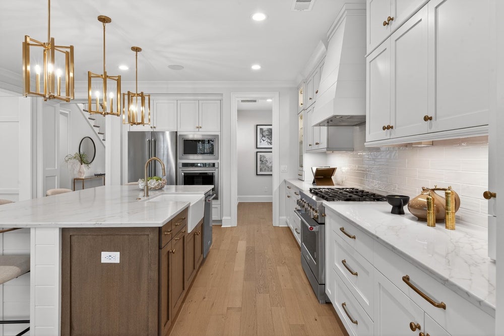 White kitchen with marble countertops, wood island, stainless appliances, and gold pendant lights