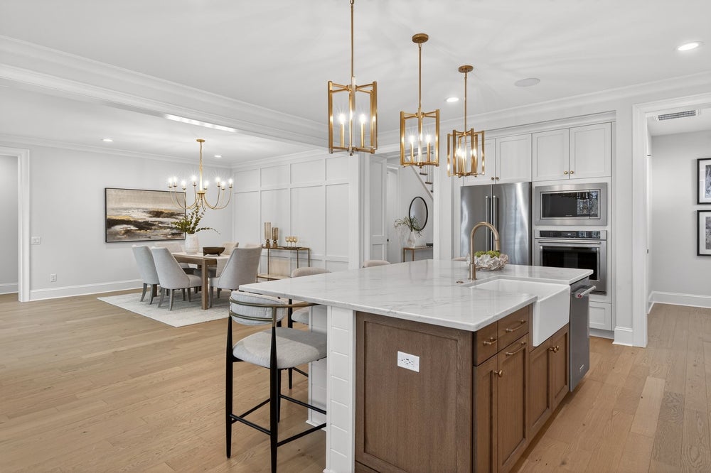 Open-concept kitchen and dining area with white cabinets, wood island, and gold pendant lights