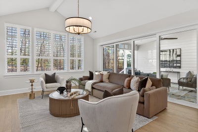 Living room with vaulted ceiling, large windows, and neutral-toned furniture on hardwood floors