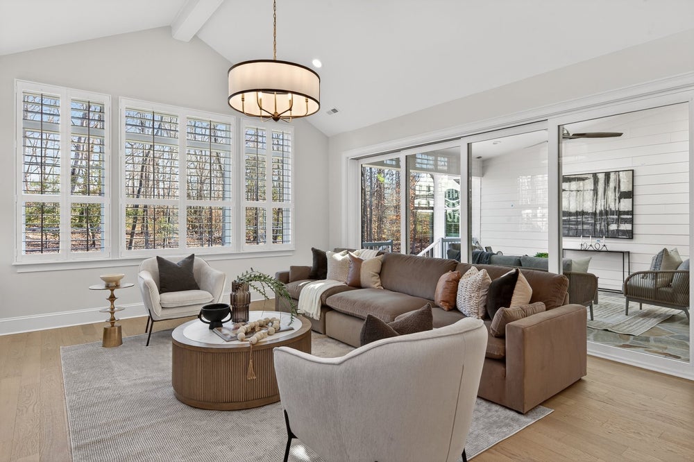 Living room with vaulted ceiling, large windows, and neutral-toned furniture on hardwood floors