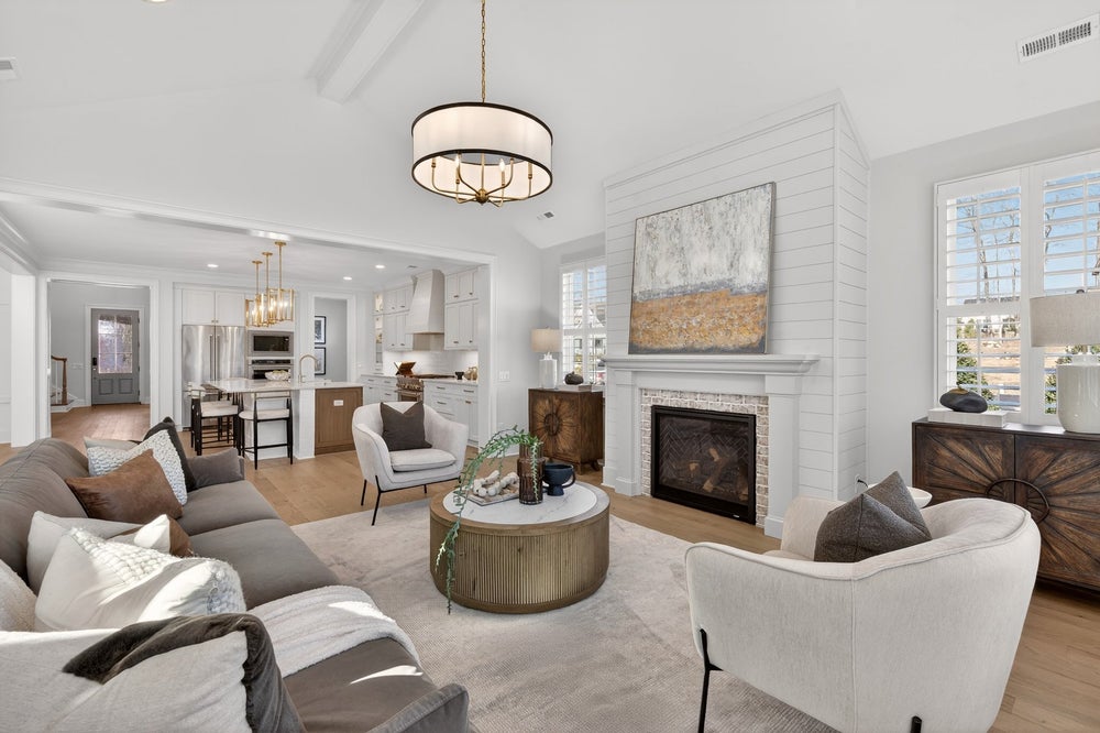 Open concept living room with white shiplap fireplace and view into kitchen with island