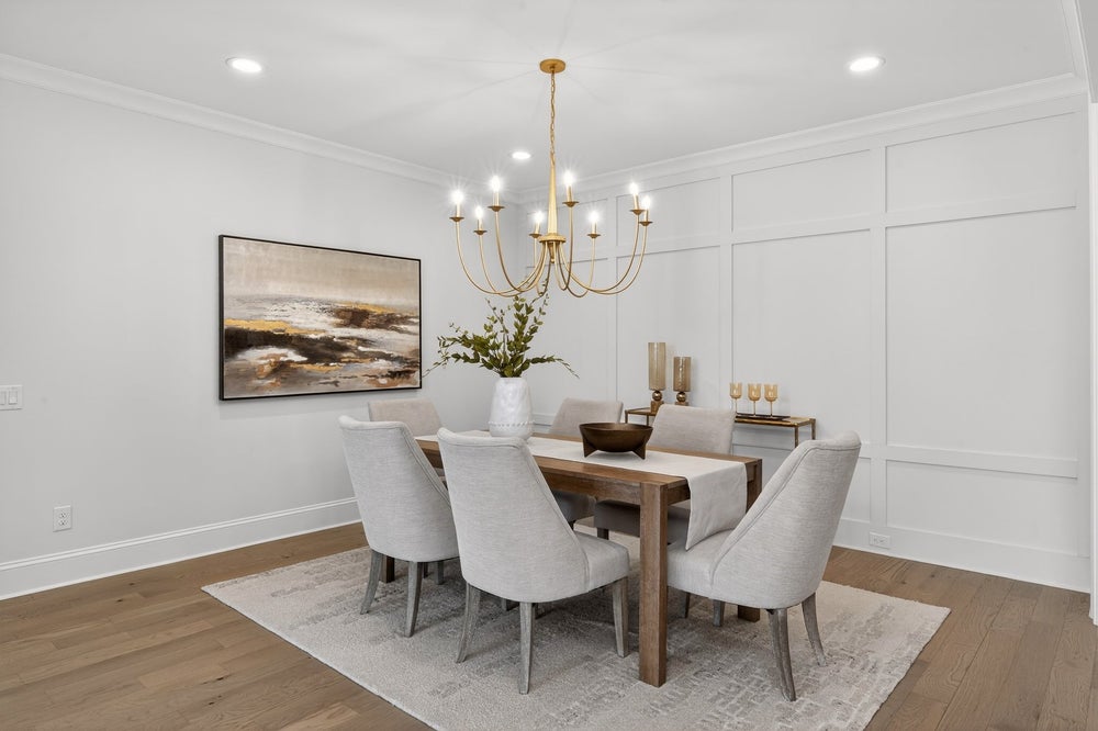 Dining room with wood table, upholstered chairs, gold chandelier, and white wainscoting