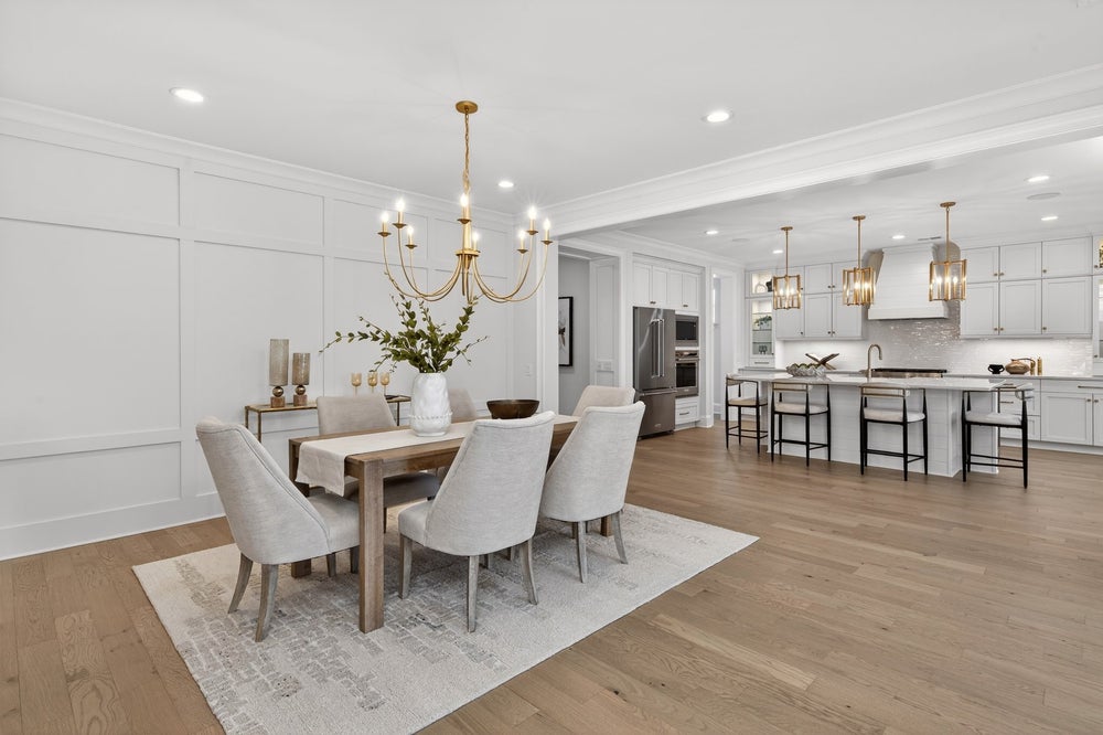 Open-concept dining room and kitchen with white cabinets, wood floors, and brass chandelier