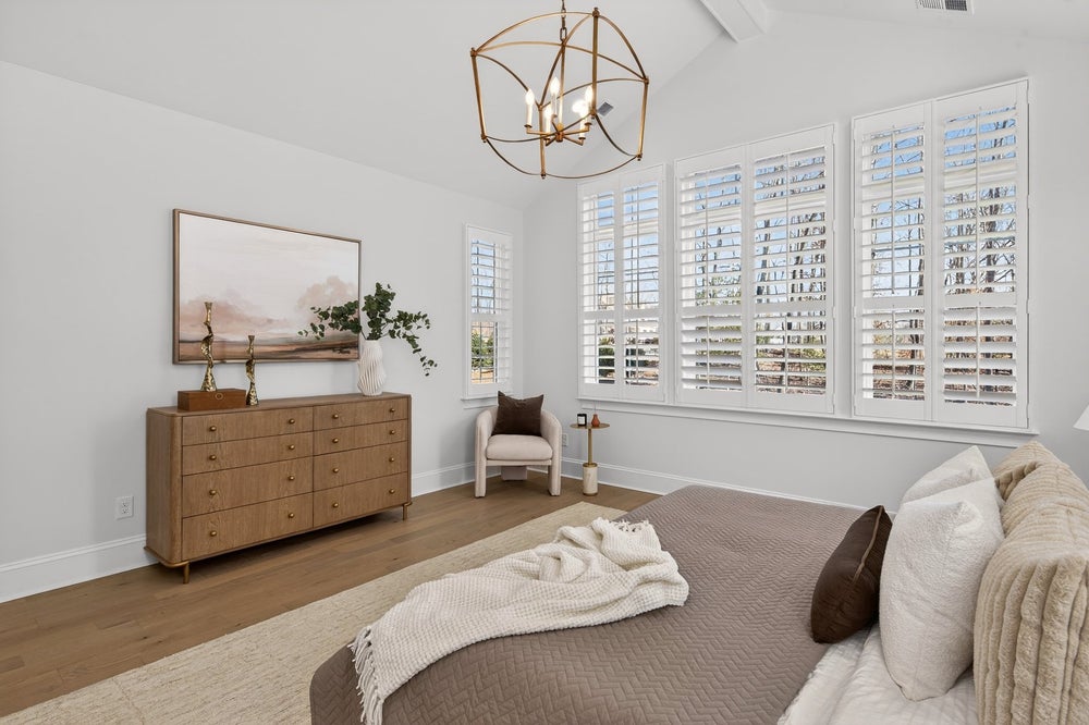Master bedroom with vaulted ceiling, white plantation shutters, and wood dresser