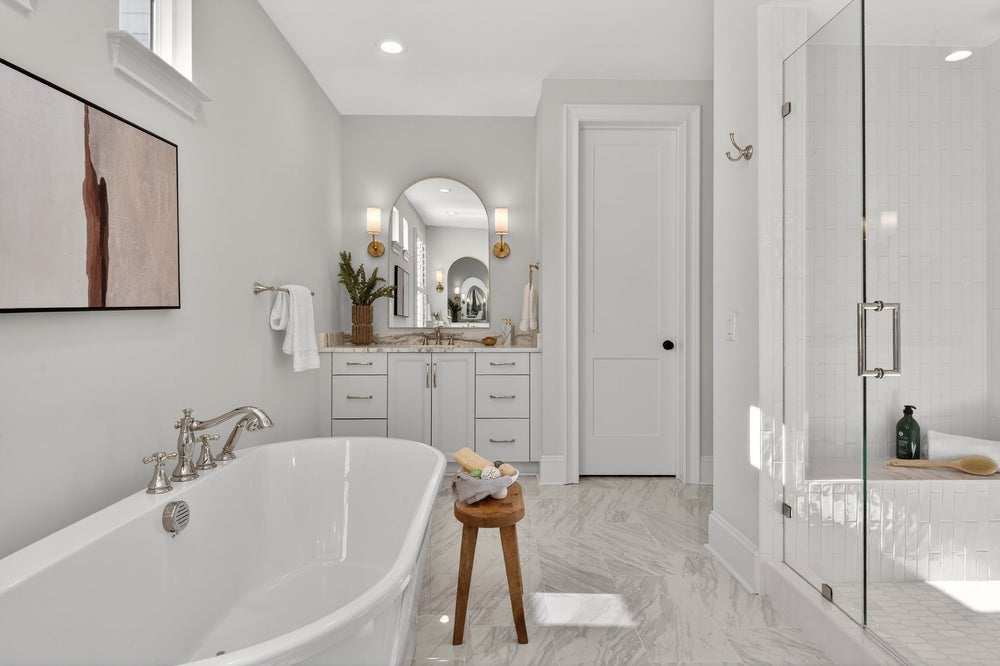Spacious bathroom with freestanding tub, white vanity, arched mirror, and glass shower enclosure