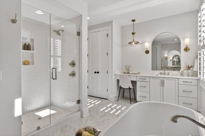 White master bathroom with glass shower, freestanding tub, vanity with makeup area, and brass fixtures