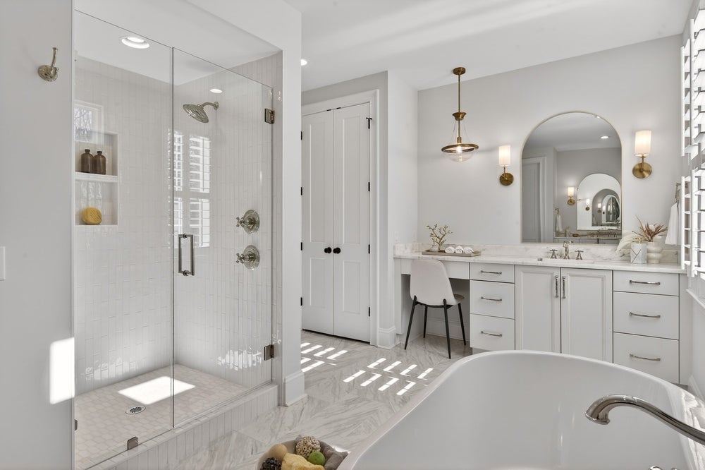 White master bathroom with glass shower, freestanding tub, vanity with makeup area, and brass fixtures