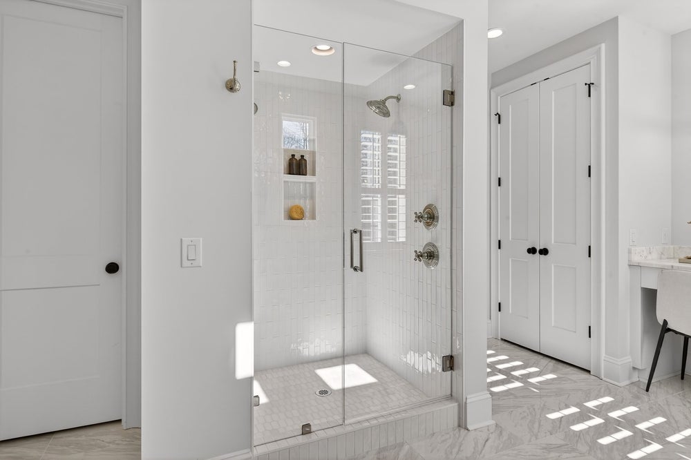 White bathroom with glass-enclosed walk-in shower, marble floors, and built-in shower niche