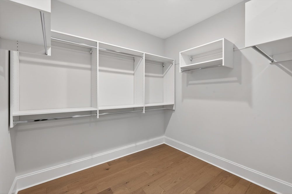Walk-in closet with white built-in shelving and hanging rods on hardwood floors