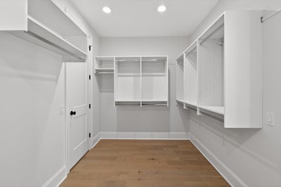 Walk-in closet with white built-in shelving, hanging rods, and hardwood flooring