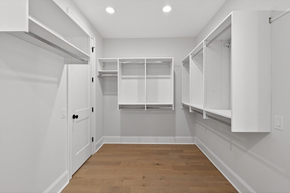 Walk-in closet with white built-in shelving, hanging rods, and hardwood flooring