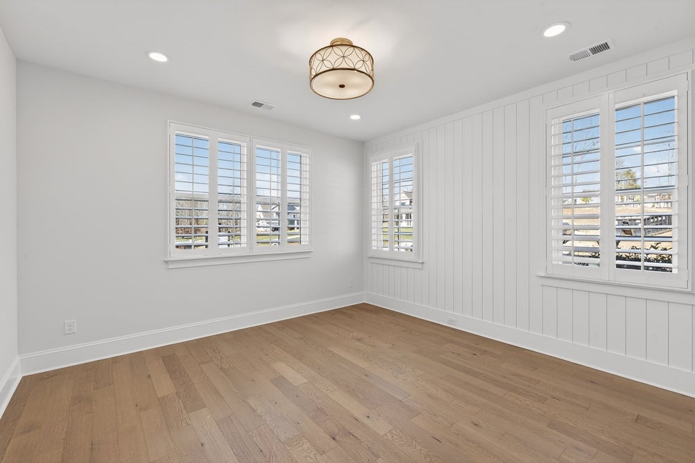 Empty room with white shiplap walls, hardwood floors, and plantation shutters on three windows