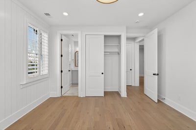 Empty bedroom with white walls, hardwood floors, built-in closet, and ensuite bathroom access
