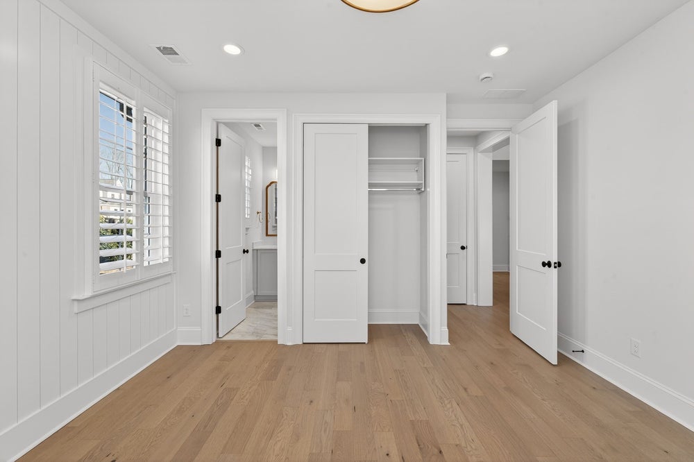 Empty bedroom with white walls, hardwood floors, built-in closet, and ensuite bathroom access