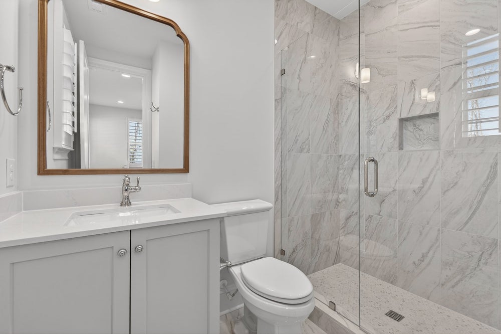 Modern bathroom with white vanity, marble tile shower, and gold-framed mirror