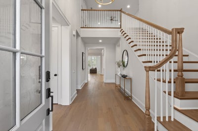 Two-story foyer with curved wooden staircase, light hardwood floors, and second-floor balcony overlook