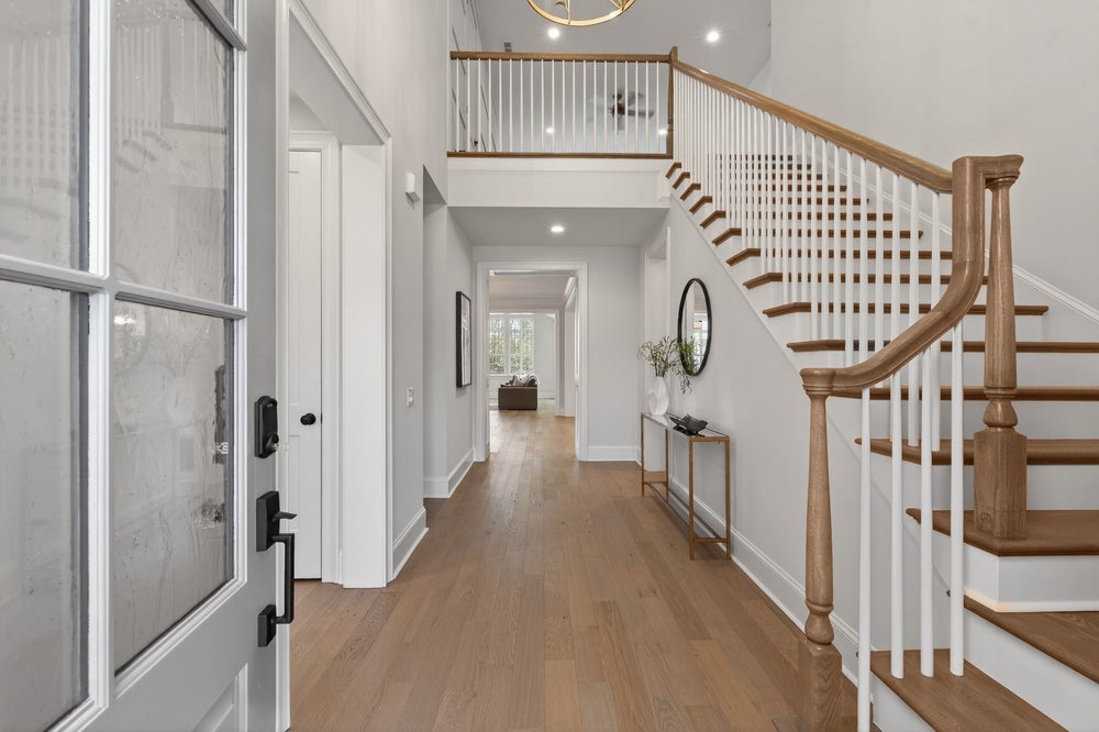 Two-story foyer with curved wooden staircase, light hardwood floors, and second-floor balcony overlook