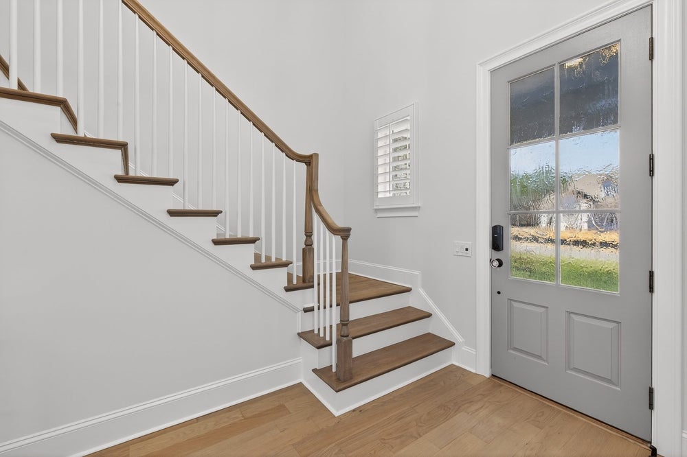 Entryway with wooden staircase, white railings, and glass-panel front door