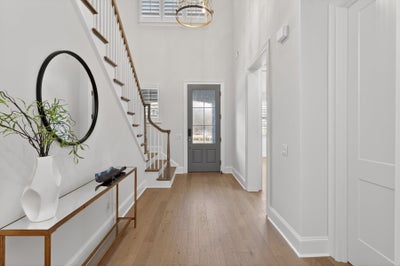 Bright entryway with light wood floors, curved staircase, and gray front door with glass panel