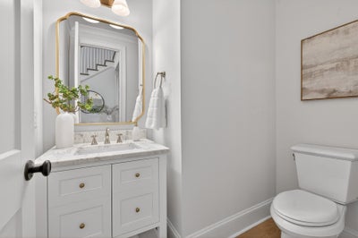Bathroom with white vanity, marble countertop, gold-framed mirror, and light gray walls