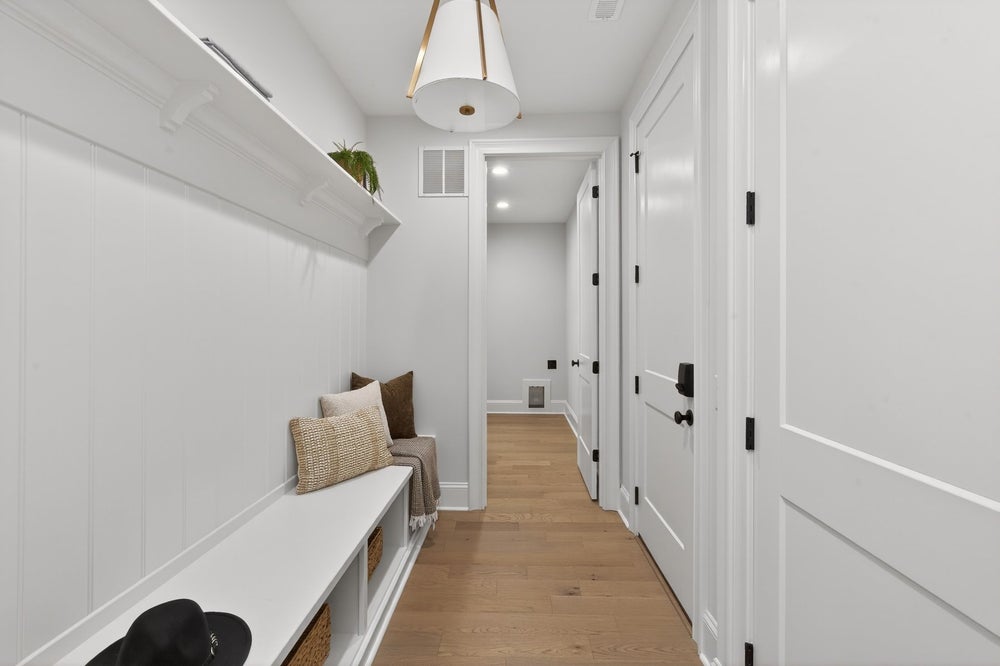 White mudroom hallway with built-in bench, storage cubbies, and light wood flooring