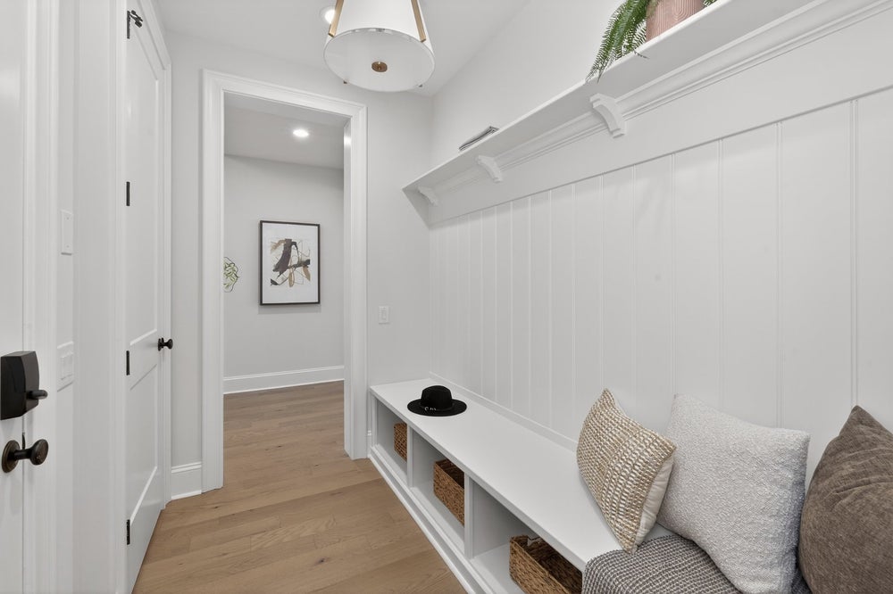 White mudroom with built-in bench, storage cubbies, and light wood flooring