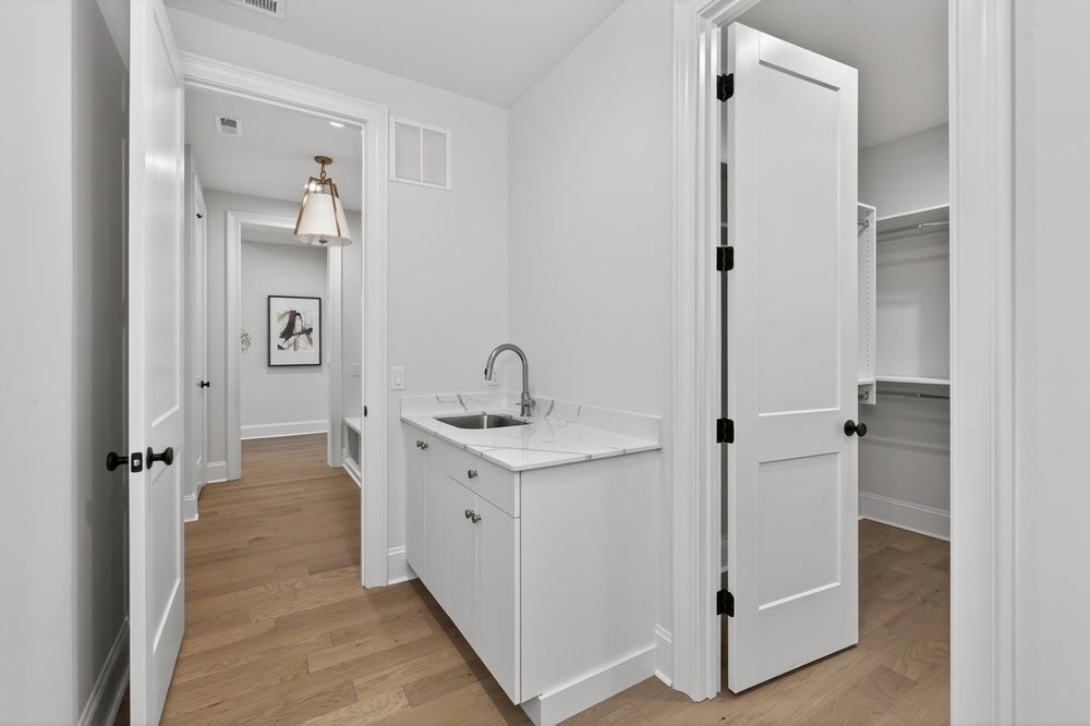 Laundry room with white cabinets, sink, and adjacent closet with hardwood floors