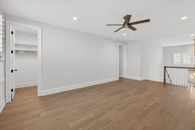 Empty room with light wood floors, white walls, ceiling fan, and walk-in closet