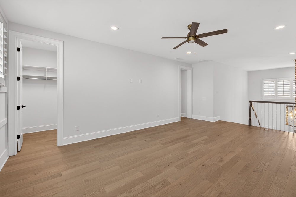 Empty room with light wood floors, white walls, ceiling fan, and walk-in closet