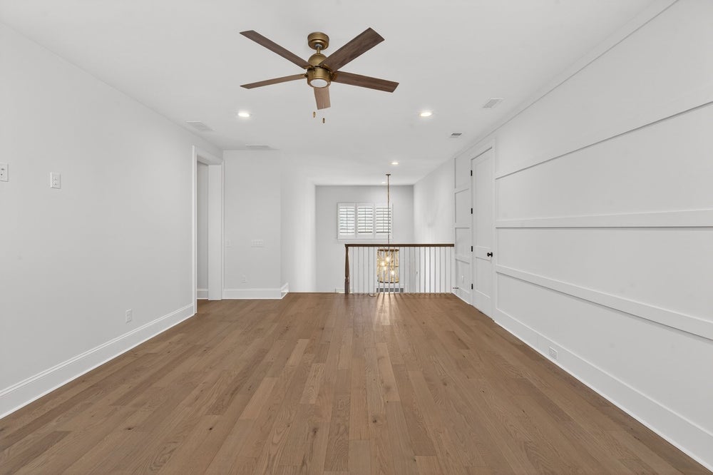 Empty upstairs room with hardwood floors, white walls, ceiling fan, and staircase railing