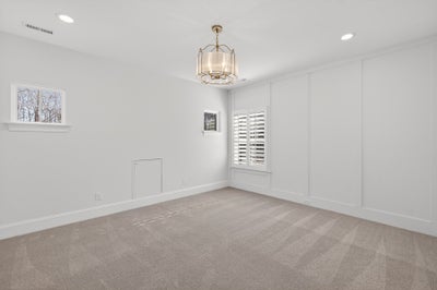 Empty bedroom with beige carpet, white walls, and decorative light fixture