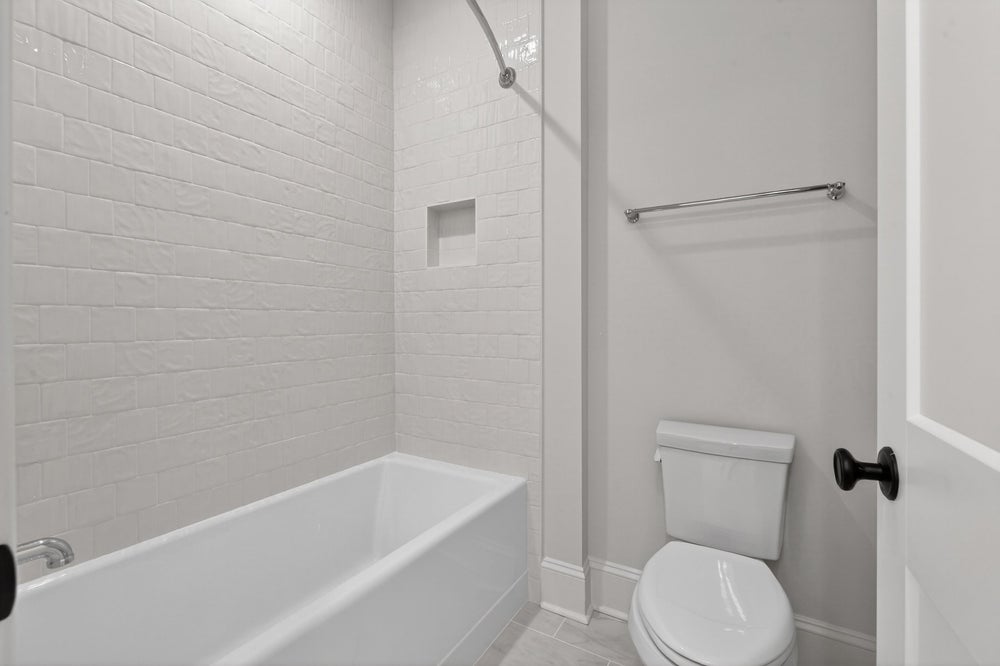 Modern bathroom with white subway tile shower, bathtub, and toilet with gray walls