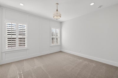 Empty bedroom with white walls, plantation shutters, and beige carpet with chandelier