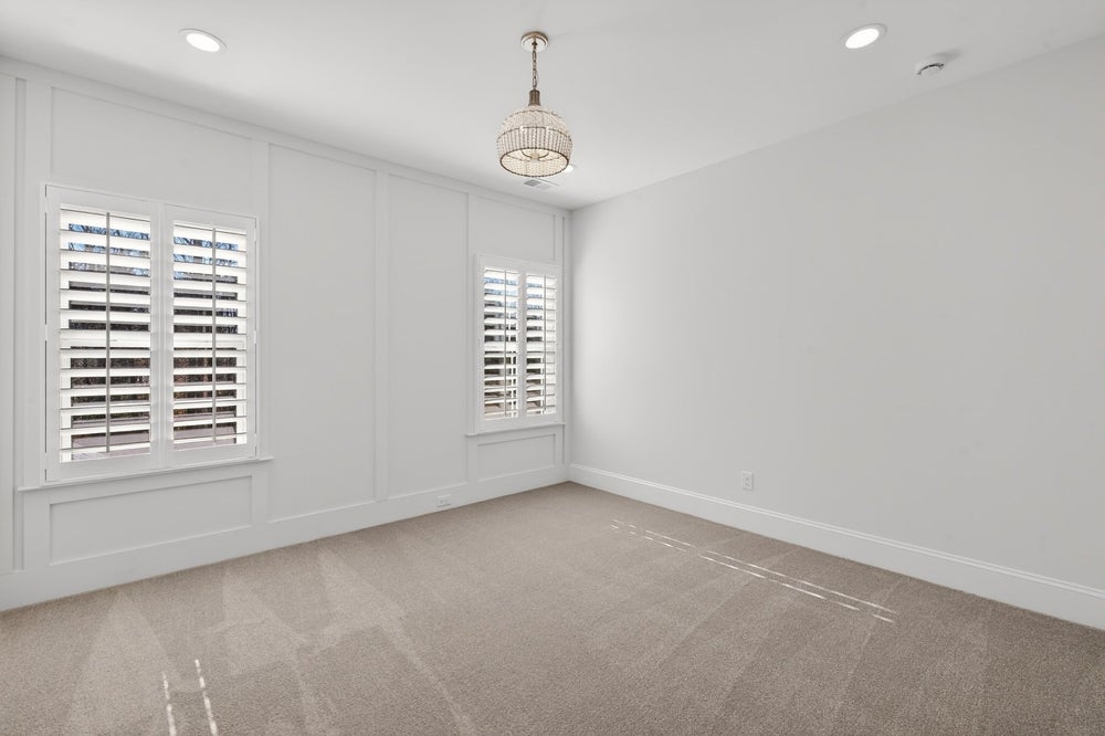 Empty bedroom with white walls, plantation shutters, and beige carpet with chandelier
