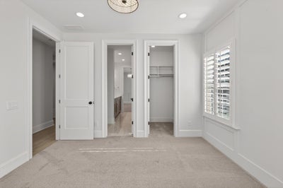 Bedroom with beige carpet, white walls, and three doorways leading to bathroom and closets