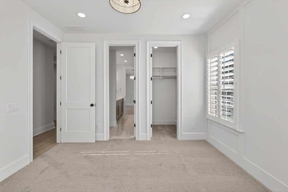 Bedroom with beige carpet, white walls, and three doorways leading to bathroom and closets