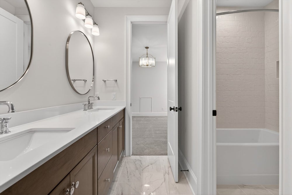 Modern bathroom with double vanity, oval mirrors, and marble tile flooring